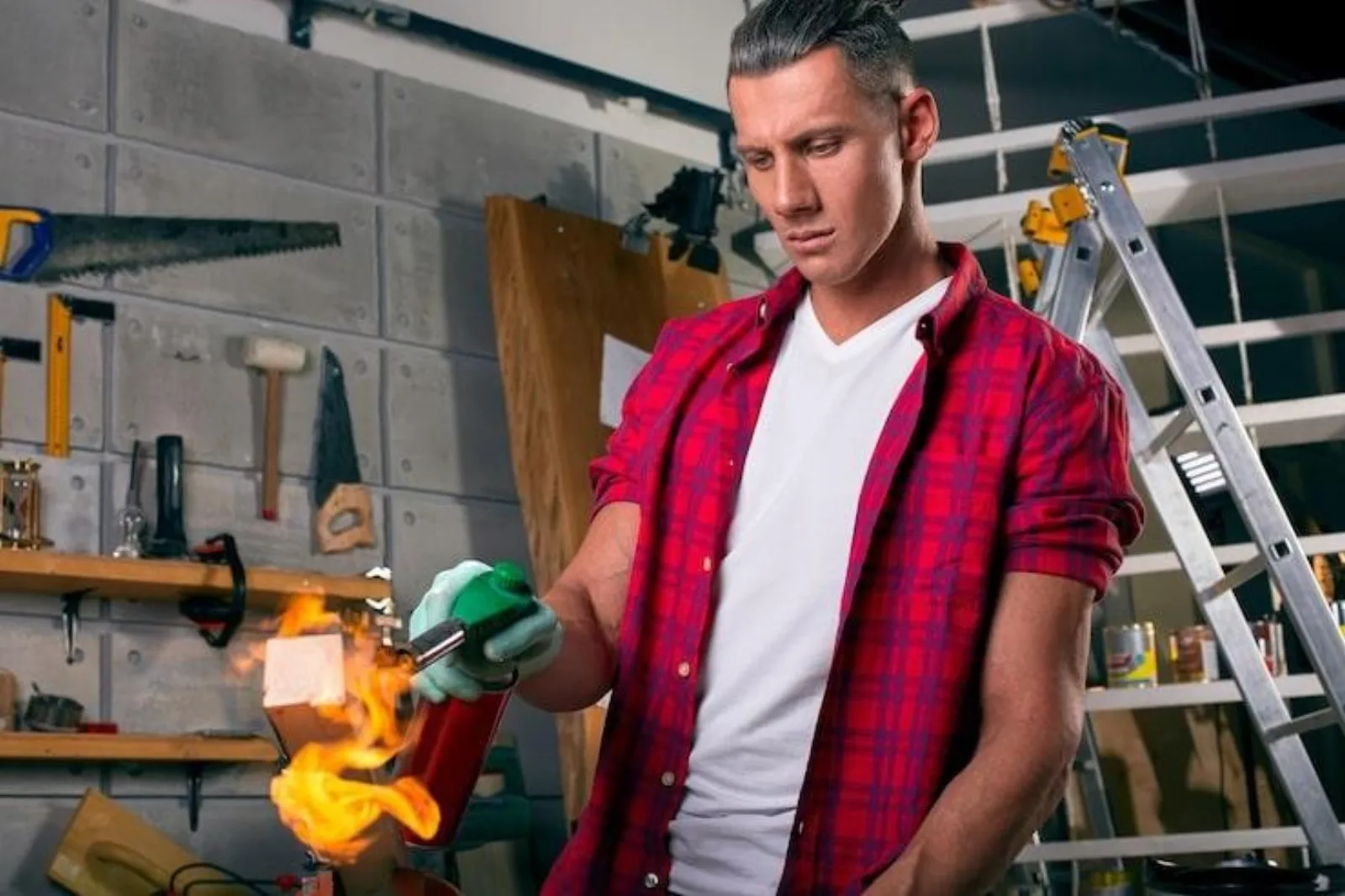 Houston handyman in a red plaid shirt using a blowtorch in the workshop while managing jobs